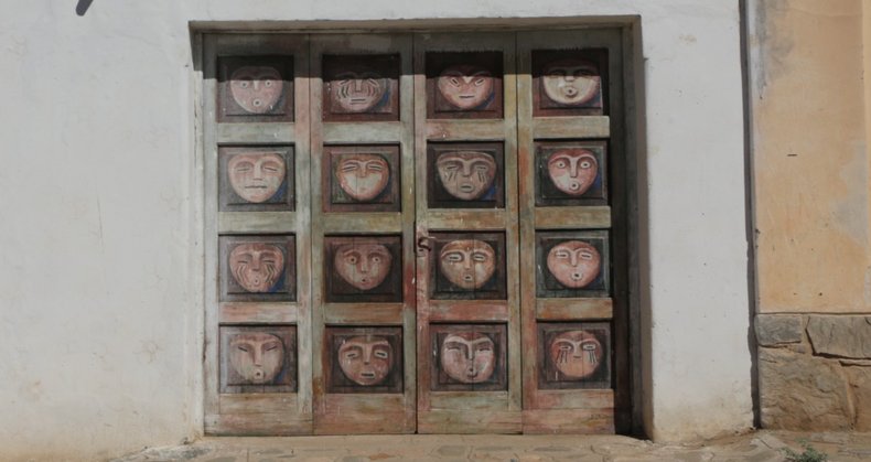 Puerta de madera pintada con rostros, en una casa de adobe de Angualasto.